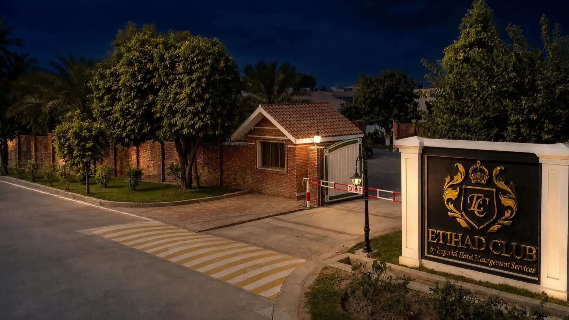 The lit entrance gate to Etihad Club, Rahim Yar Khan, its crest on the wall beside the drive