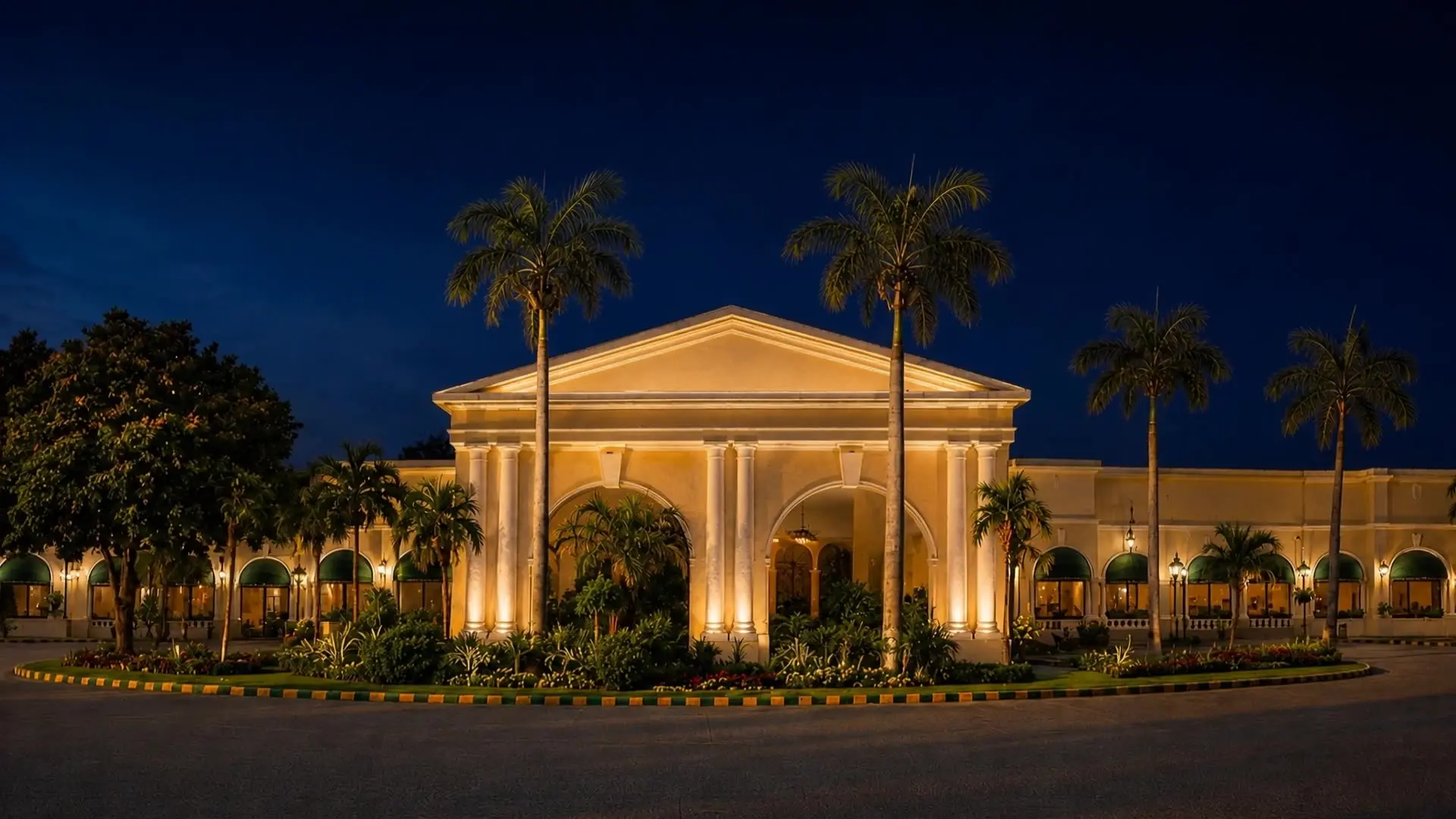 The portico of Faletti’s Hotel Lahore at night, lit gold between the palms