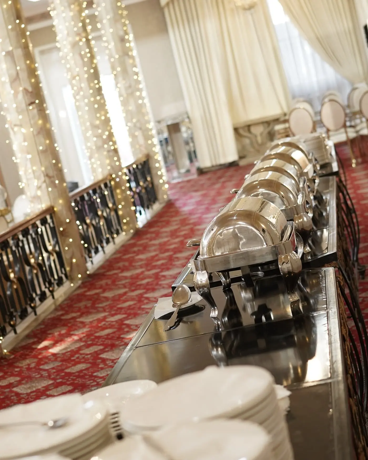 A buffet line of covered chafing dishes with plates set out at The Palace Banquet