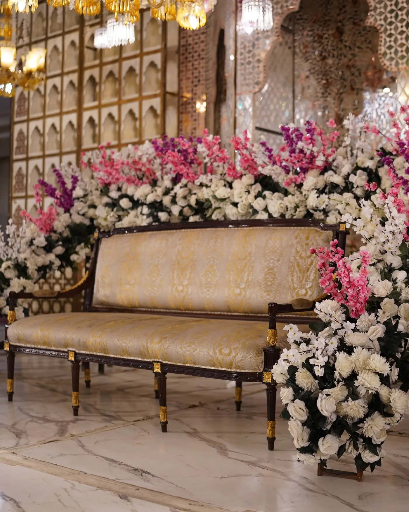 A gilded sofa set with blossom arrangements against a mirrored screen